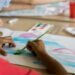 child watercolor painting an ocean scene at the table with various watercolor paints in front of him