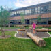 Girl walking outside across log in front of school building.