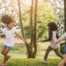 Girls running around outside by trees.