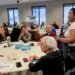 room of people sitting at round tables as part of the nature everywhere vision labs. One woman is standing up smiling