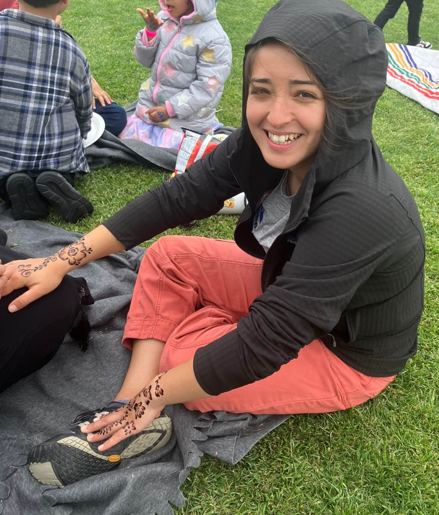 woman smiling at camera as she gets henna tattoos on her hands in the park