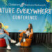 Two members of the 2024 Youth Advisory Council sit in chairs and laugh while chatting on a stage.