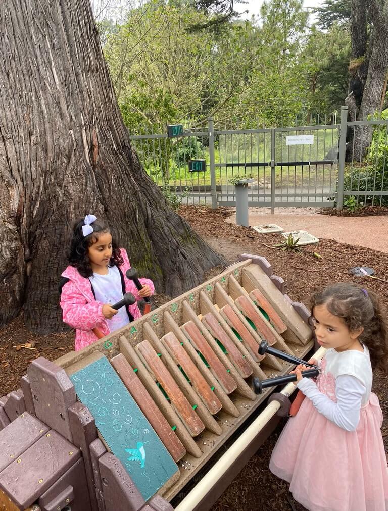 two children playing xylophone feature in outdoor park