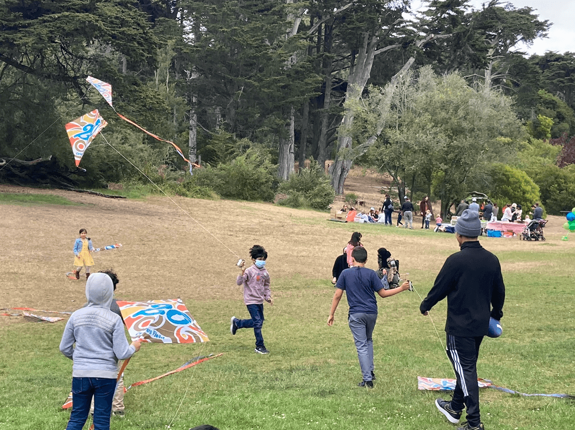 group of children running around open grass field with kites. Some kites are flying while others are still on the ground.
